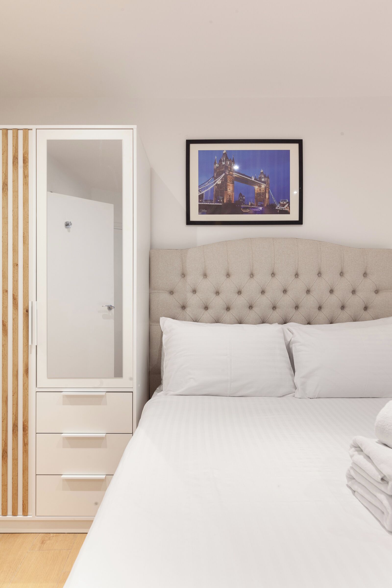 Ein Schlafzimmer mit einem großen Bett, einem weißen Kleiderschrank und einem gerahmten Bild einer Brücke an der Wand.