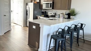 Une cuisine moderne dotée d’un îlot central, d’appareils électroménagers en acier inoxydable et de tabourets de bar.