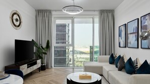 Ein modernes Wohnzimmer mit Flachbildfernseher, rundem Couchtisch, Sofa und großem Fenster mit Blick auf die Stadt.