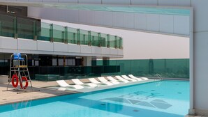 Ein moderner, überdachter Pool mit klarem, blauen Wasser, einer Glasbrüstung und einer weißen Lounge-Bereich mit Liegestühlen.