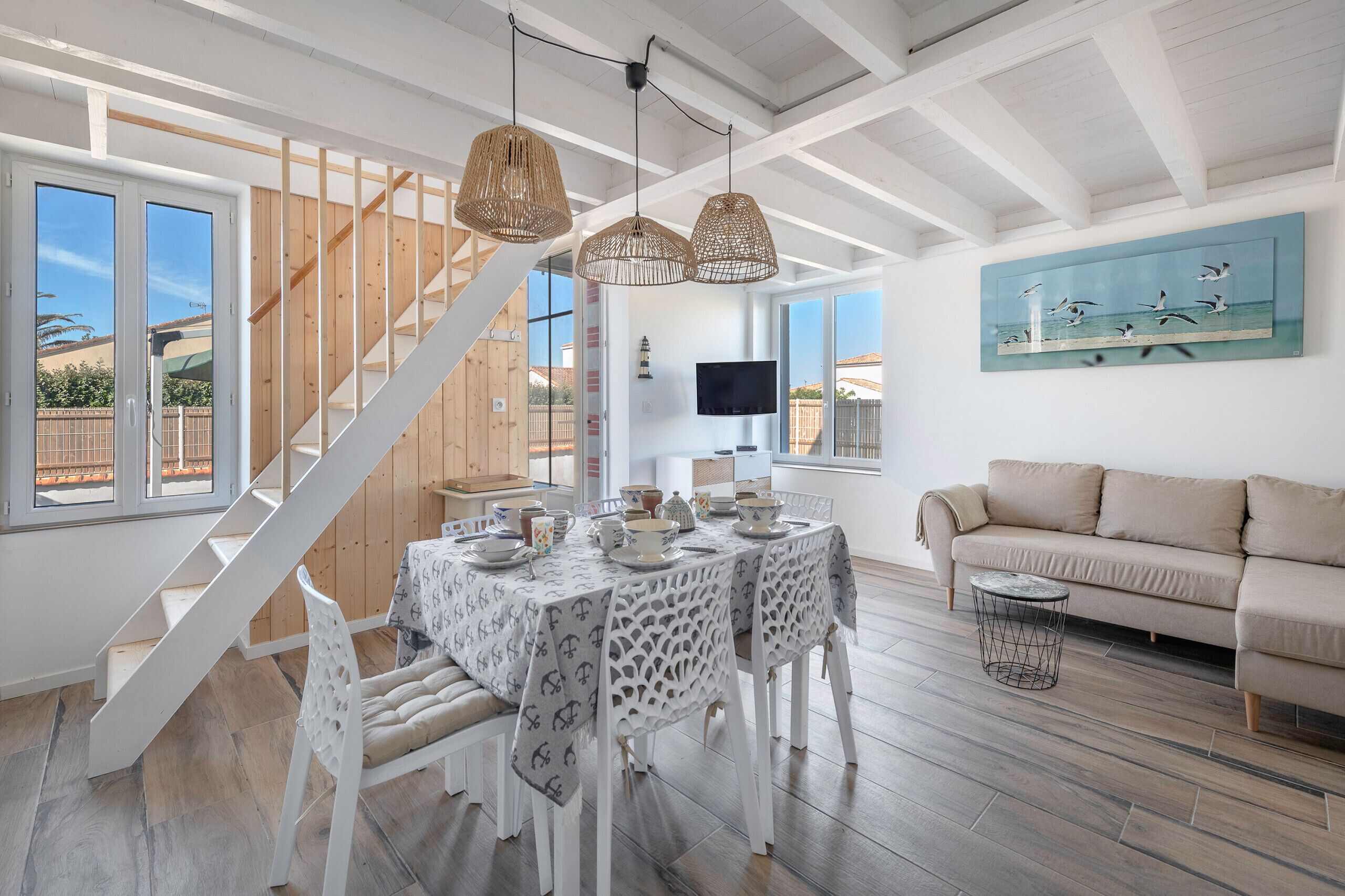 Un amplio espacio de sala con una escalera, una mesa de comedor dispuesta con vajilla y un sofá.