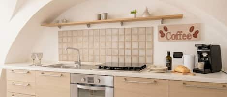 A modern kitchen with a built-in oven, a coffee machine, and a shelf with kitchenware.