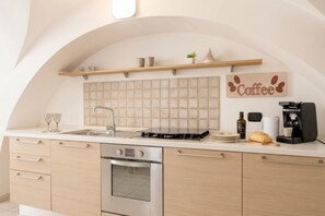 A modern kitchen with a built-in oven, a coffee machine, and a shelf with kitchenware. - The Suite - Cozy Apartment (Bari)