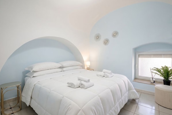 A bedroom with a bed, pillows, a nightstand, a lamp, a window with a view, and a plant.