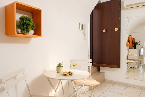 A room with a white round table, a potted plant, a small plate of snacks, a white chair, a wooden door, and a white wall-mounted phone. - The Suite - Cozy Apartment (Bari)