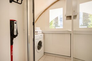 A laundry area with a washing machine, a red vacuum cleaner, and a window with a view of buildings. - The Suite - Cozy Apartment (Bari)