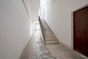 Un couloir étroit avec un escalier menant à une porte au fond.