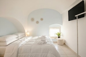 A bedroom with a bed, a TV mounted on the wall, and a window with a plant.