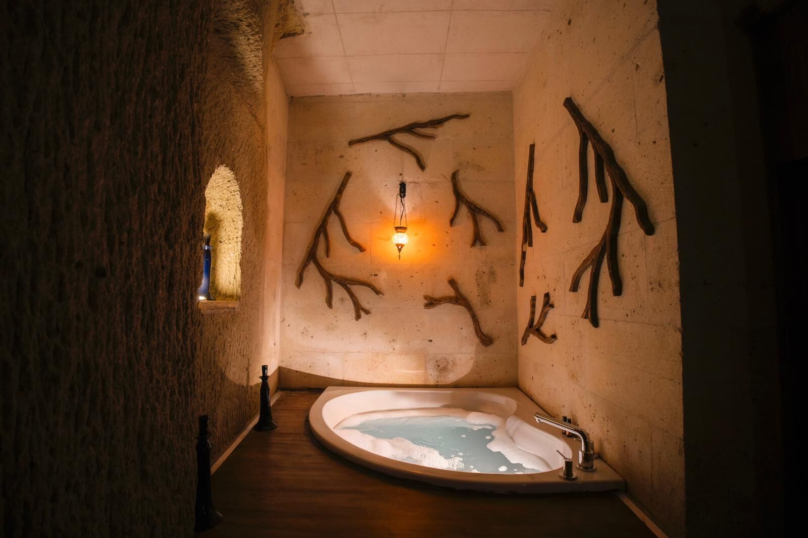 A spa room with a wooden floor, a bathtub, and wall-mounted branches.