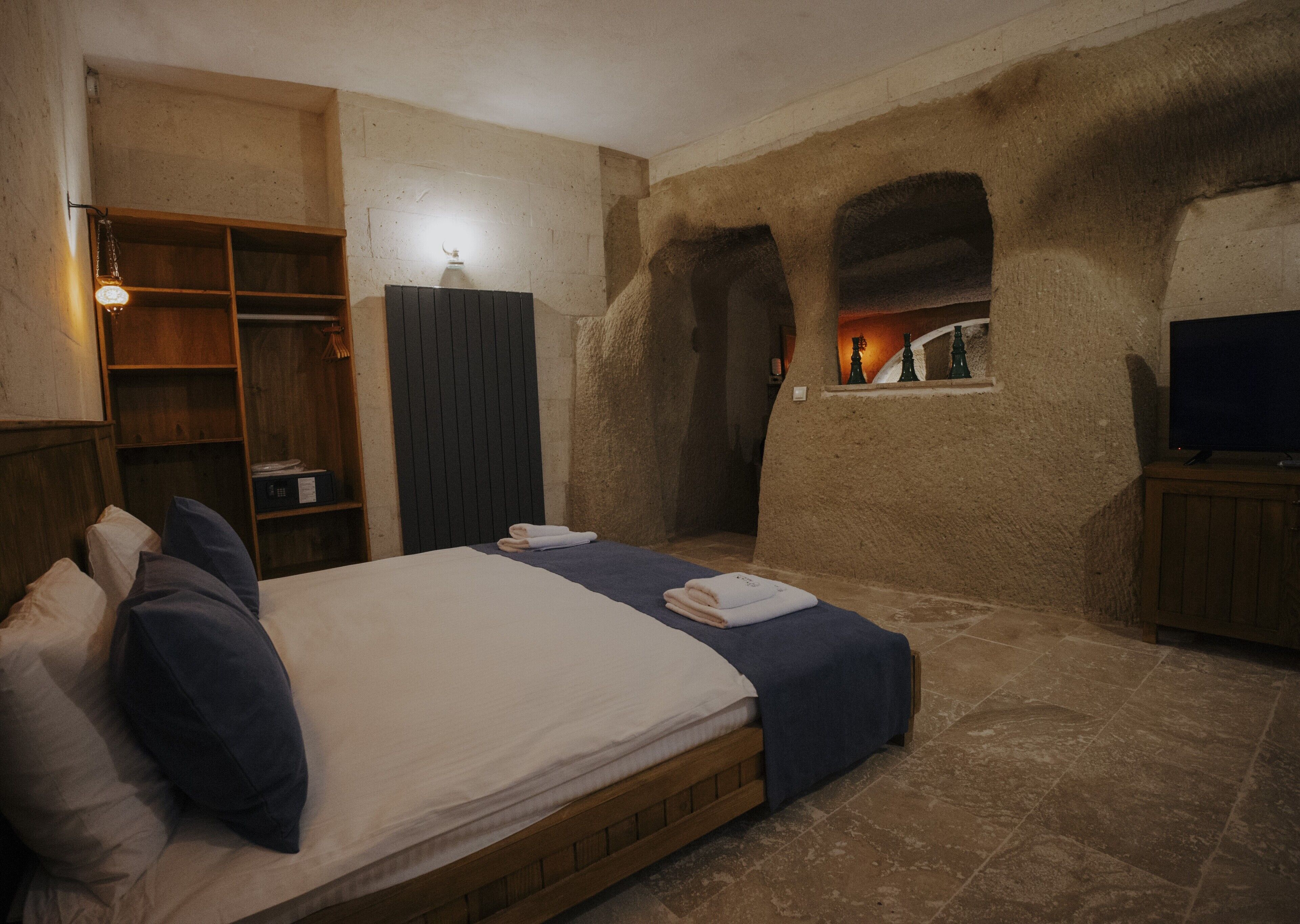 A bedroom with a wooden bed, a wardrobe, a television, and a stone wall with a window.