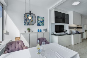 Una cocina moderna con muebles blancos, un área de comedor con mesa y sillas, y obras de arte en las paredes.