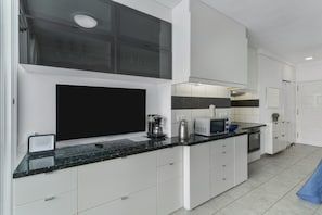 Una cocina moderna con armarios blancos, una encimera negra, una cafetera y un microondas.