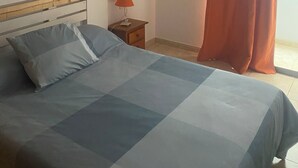 Une chambre à coucher comprenant un lit, une table de chevet, une lampe, une fenêtre avec des rideaux et une étagère fixée au mur.
