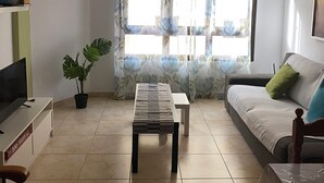 Un salon avec un canapé, une table basse, un téléviseur et une plante en pot.
