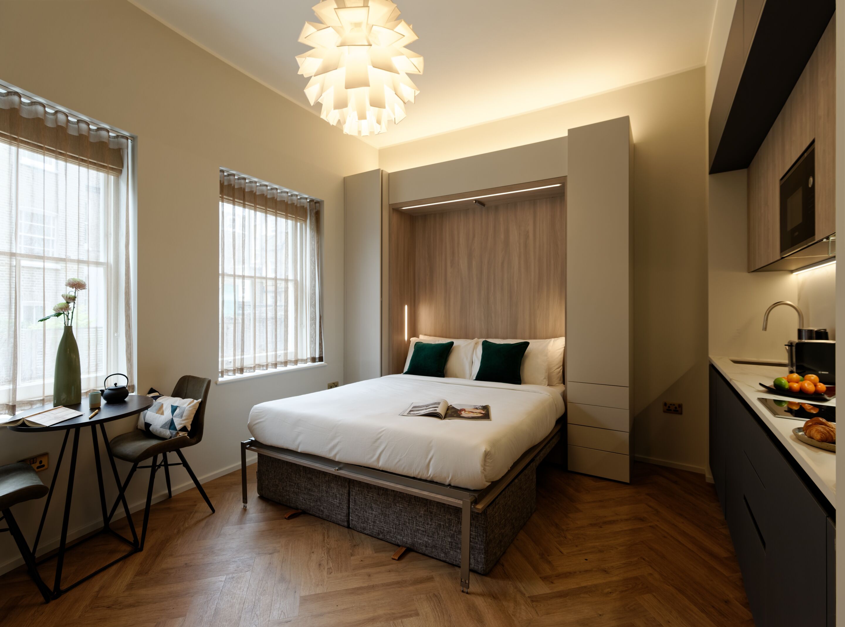 A modern bedroom with a large bed, bedside tables, a desk, and a view of the city through large windows.