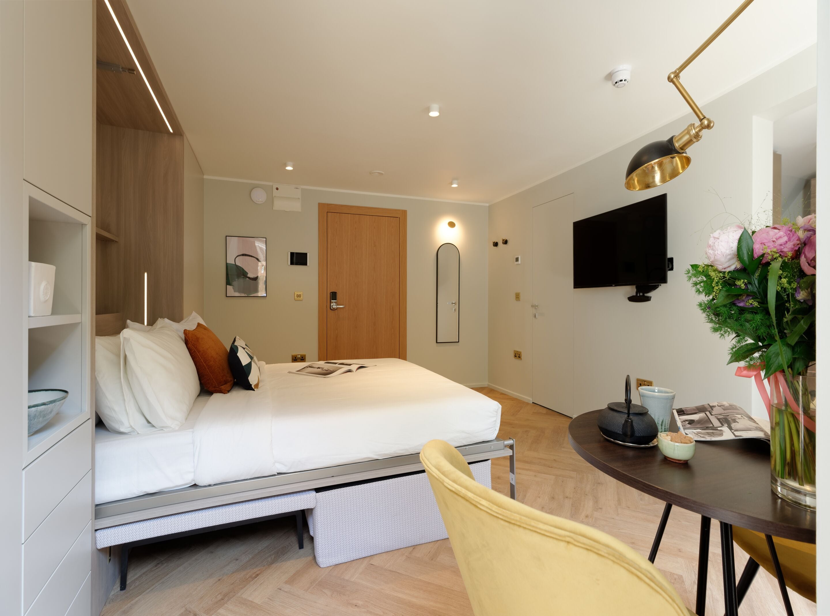 Ein modernes Hotelzimmer mit Bett, Nachttisch, Sessel und einem Flachbildfernseher.