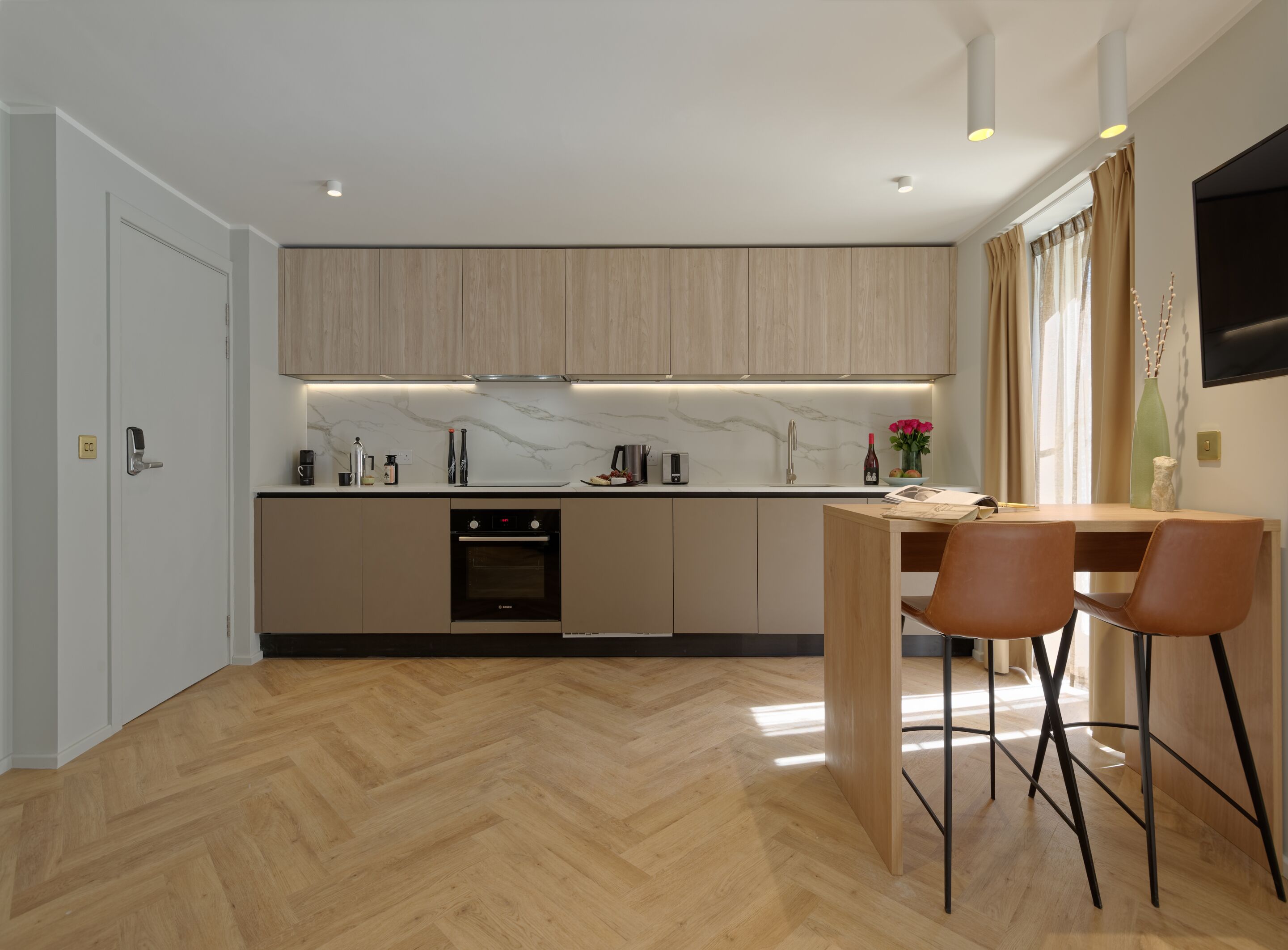 A modern kitchen with wooden cabinets, a built-in oven, and a dining area with two chairs.
