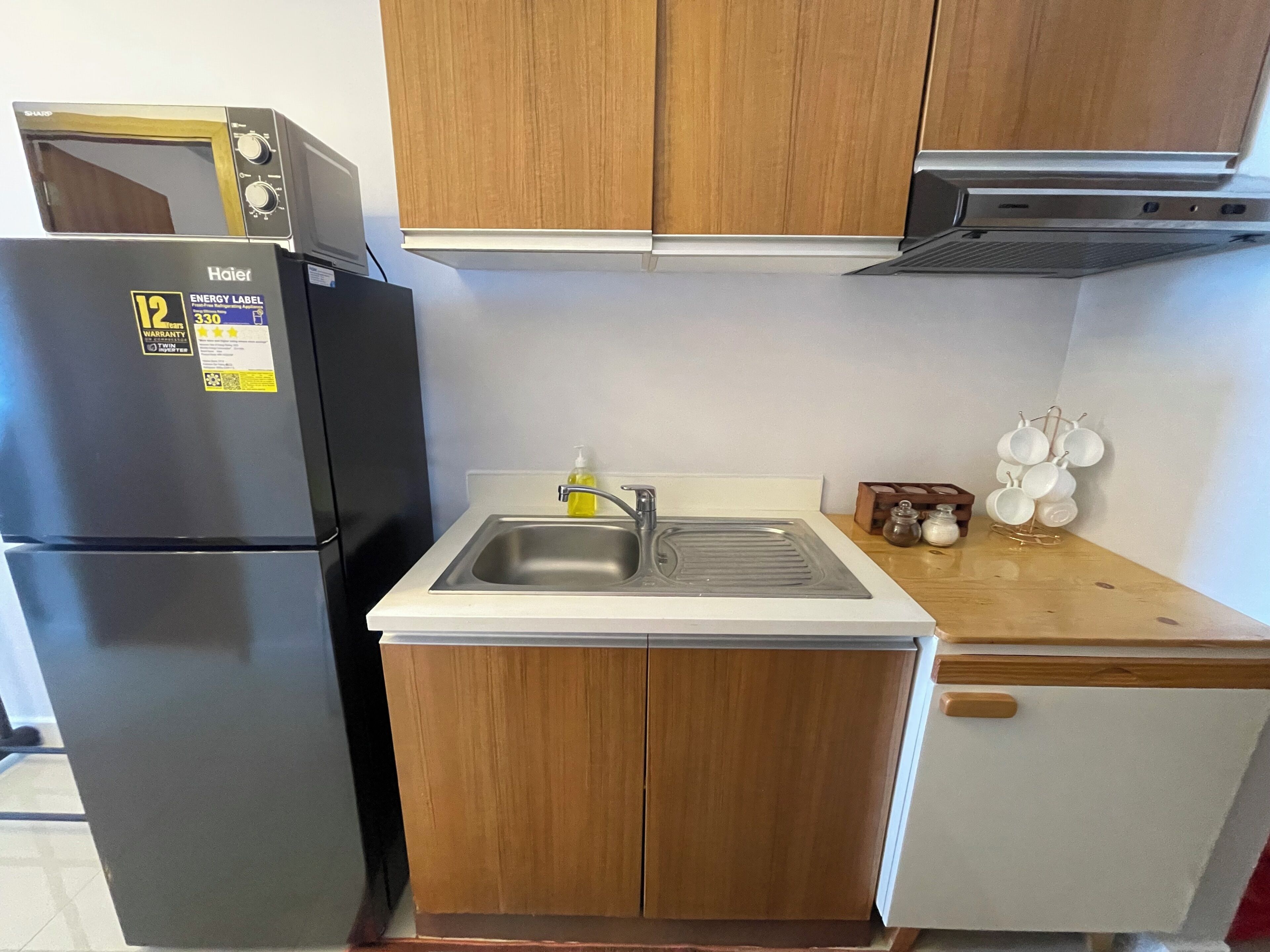 A compact kitchen with a refrigerator, a sink, wooden cabinets, and a microwave.