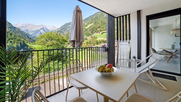 Un balcón con una mesa, sillas, un cuenco de fruta y vistas a colinas y montañas verdes.