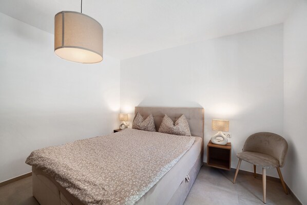 A bedroom with a bed, bedside lamps, a chair, and a hanging light fixture.