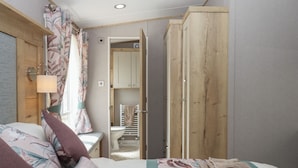 A bedroom with a bed, a wooden wardrobe, a bathroom with a toilet and a shower, and a small hallway. - Maple Lodge (Newton Abbot)