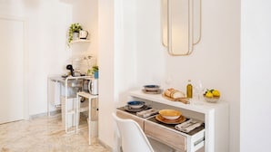 A modern kitchen with white cabinetry, a marble floor, and a dining area with a white chair and a small table. - AuGuStea Urban Studio (Bari)