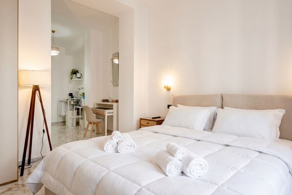 A hotel room with a bed, a desk, a chair, a lamp, and a mirror.