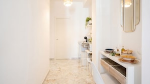 A hallway with a marble floor, a white door, a white counter with a mirror, and a pendant light. - AuGuStea Urban Studio (Bari)