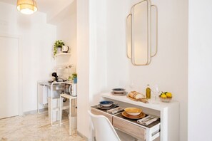 A modern kitchen with white cabinetry, a marble floor, and a dining area with a white chair and a small table.