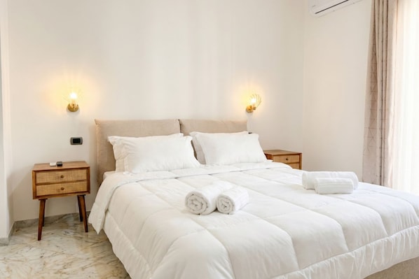 A neatly made bed with white linens, two bedside tables with wall-mounted lamps, and a marble floor.