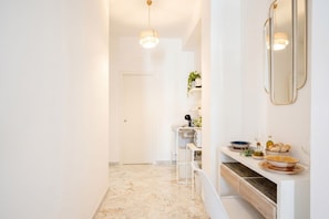 A hallway with a marble floor, a white door, a white counter with a mirror, and a pendant light.