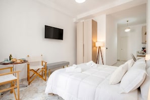 A hotel room with a bed, a desk with a chair, a TV, a lamp, and a bathroom visible through an open door.