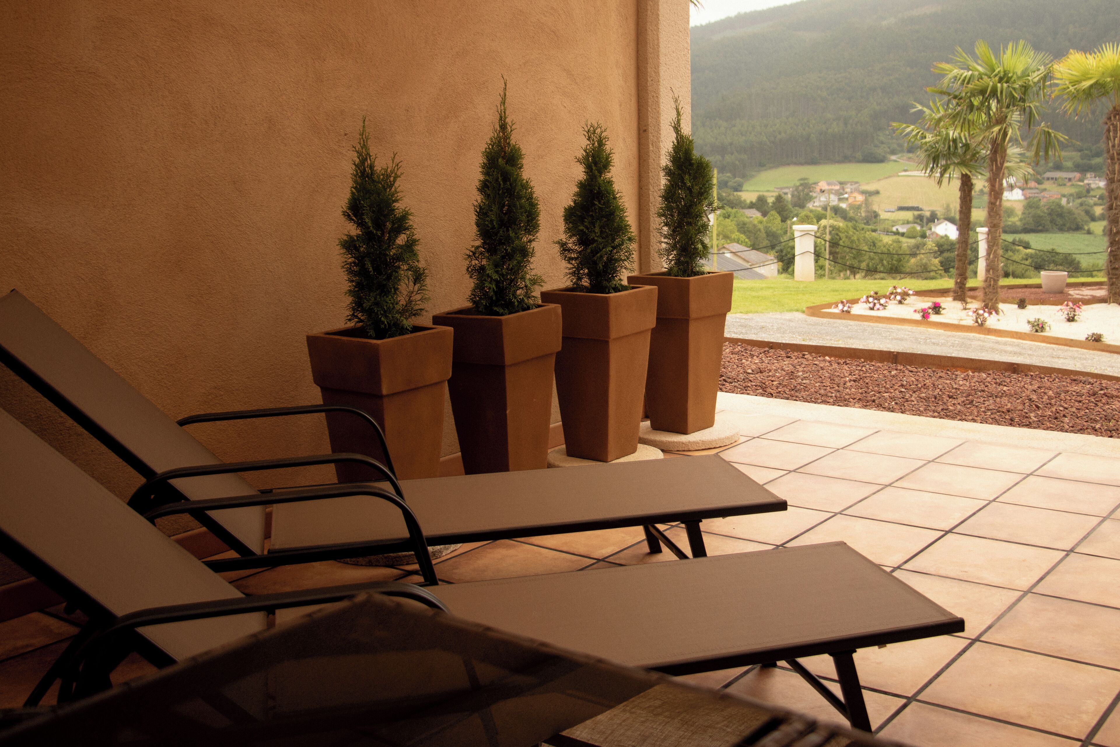 A terrace with lounge chairs and potted plants, overlooking a scenic landscape.
