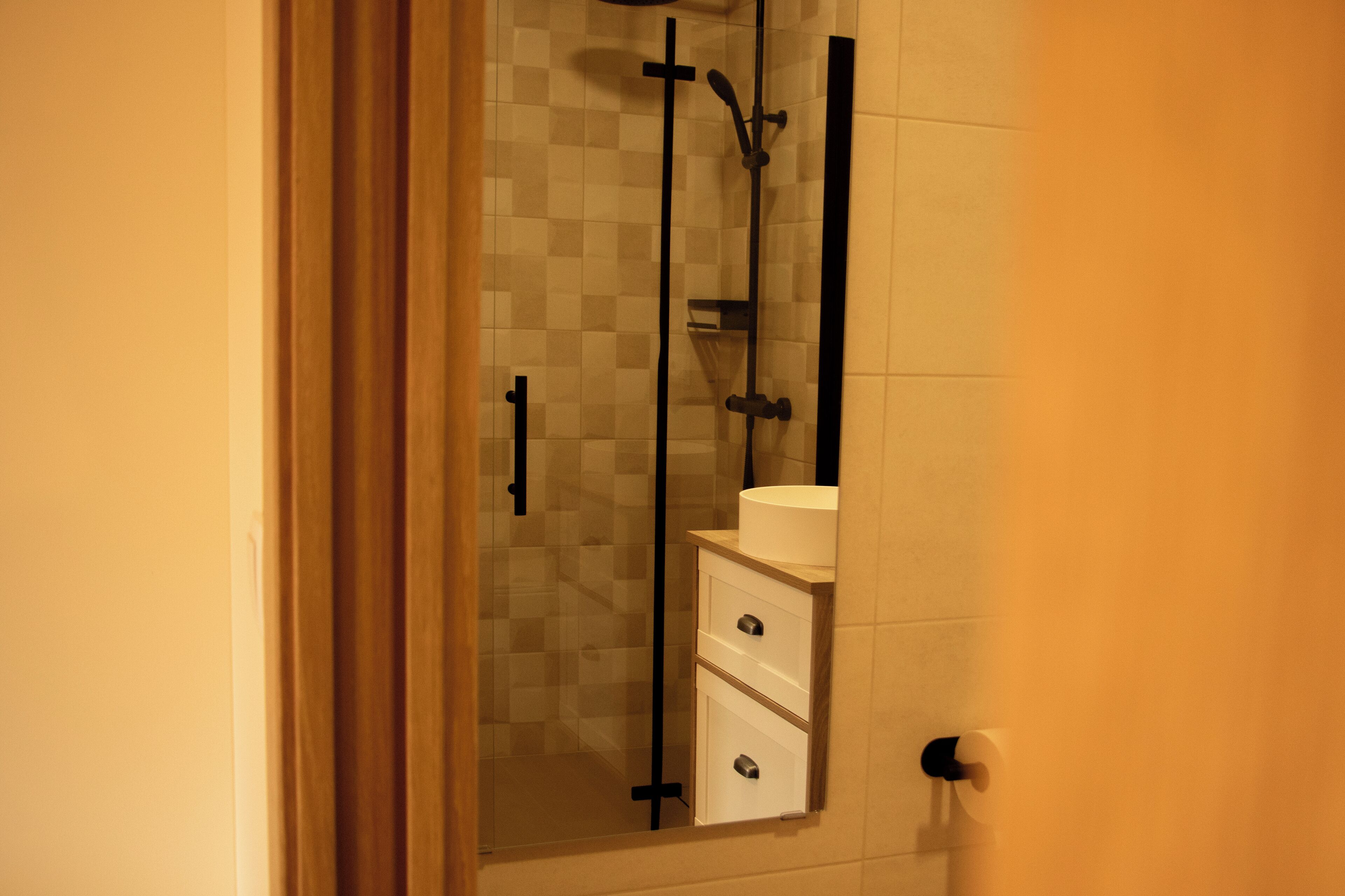 A bathroom with a glass shower enclosure, a white sink, and a wooden cabinet.