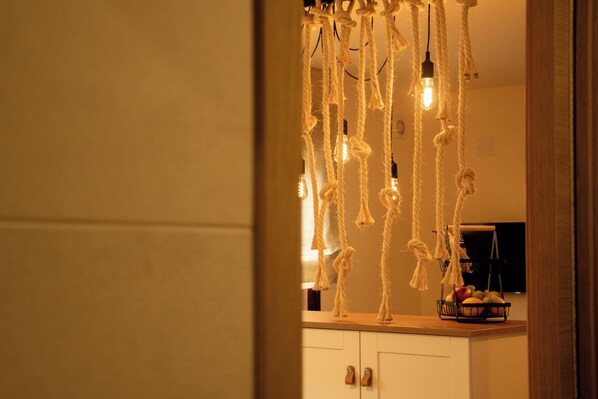 A kitchen with wooden cabinets, a fruit basket, and a hanging light fixture with exposed bulbs. - Saíñas 24 (Barreiros)