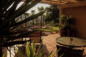 A patio area with a round glass table and chairs, surrounded by potted plants and a well-maintained lawn. - Saíñas 24 (Barreiros)