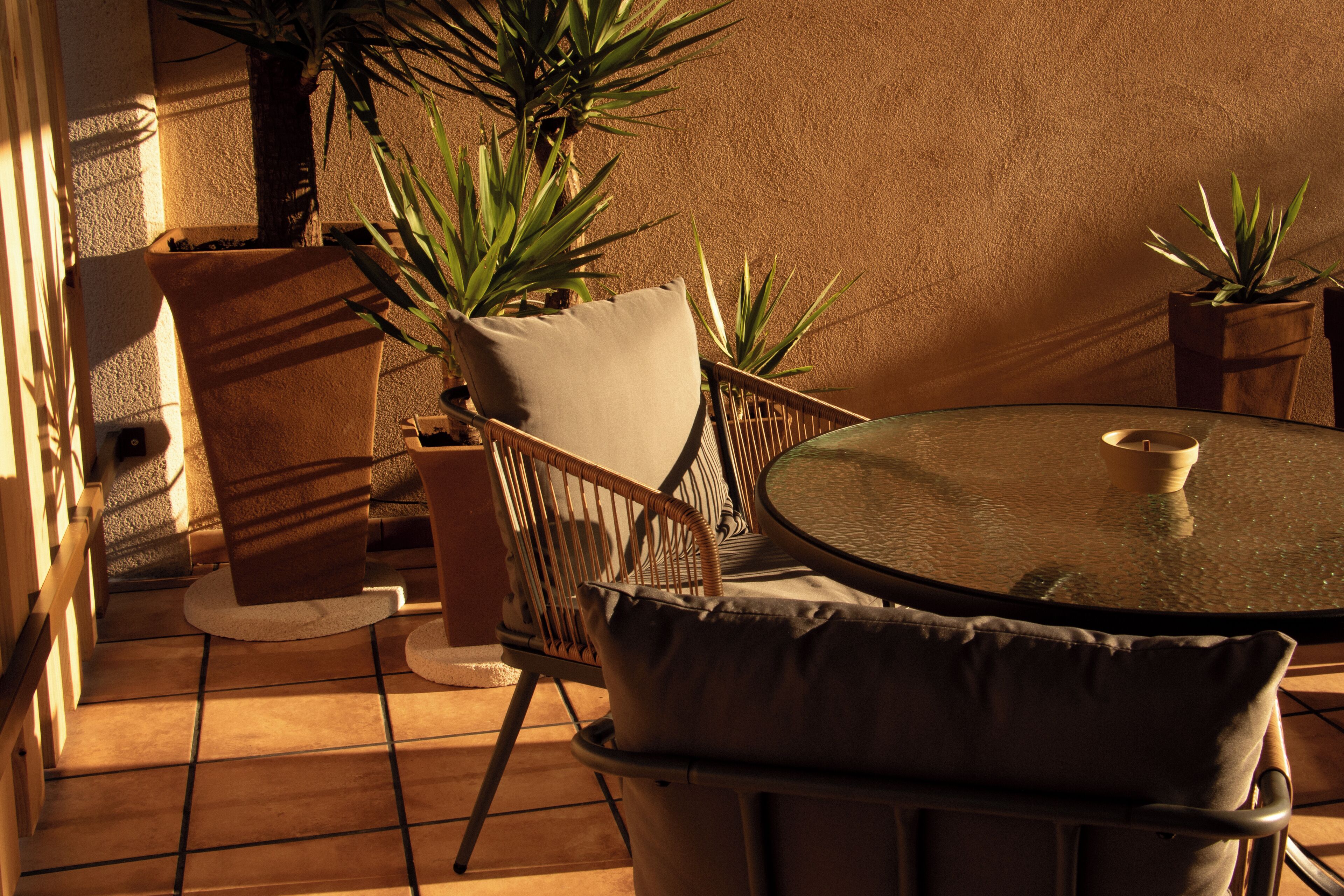 Une terrasse avec une table ronde en verre, des chaises en osier et des plantes en pot.