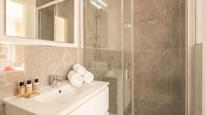 A modern bathroom with a glass-enclosed shower, a white sink with toiletries, and a large mirror.