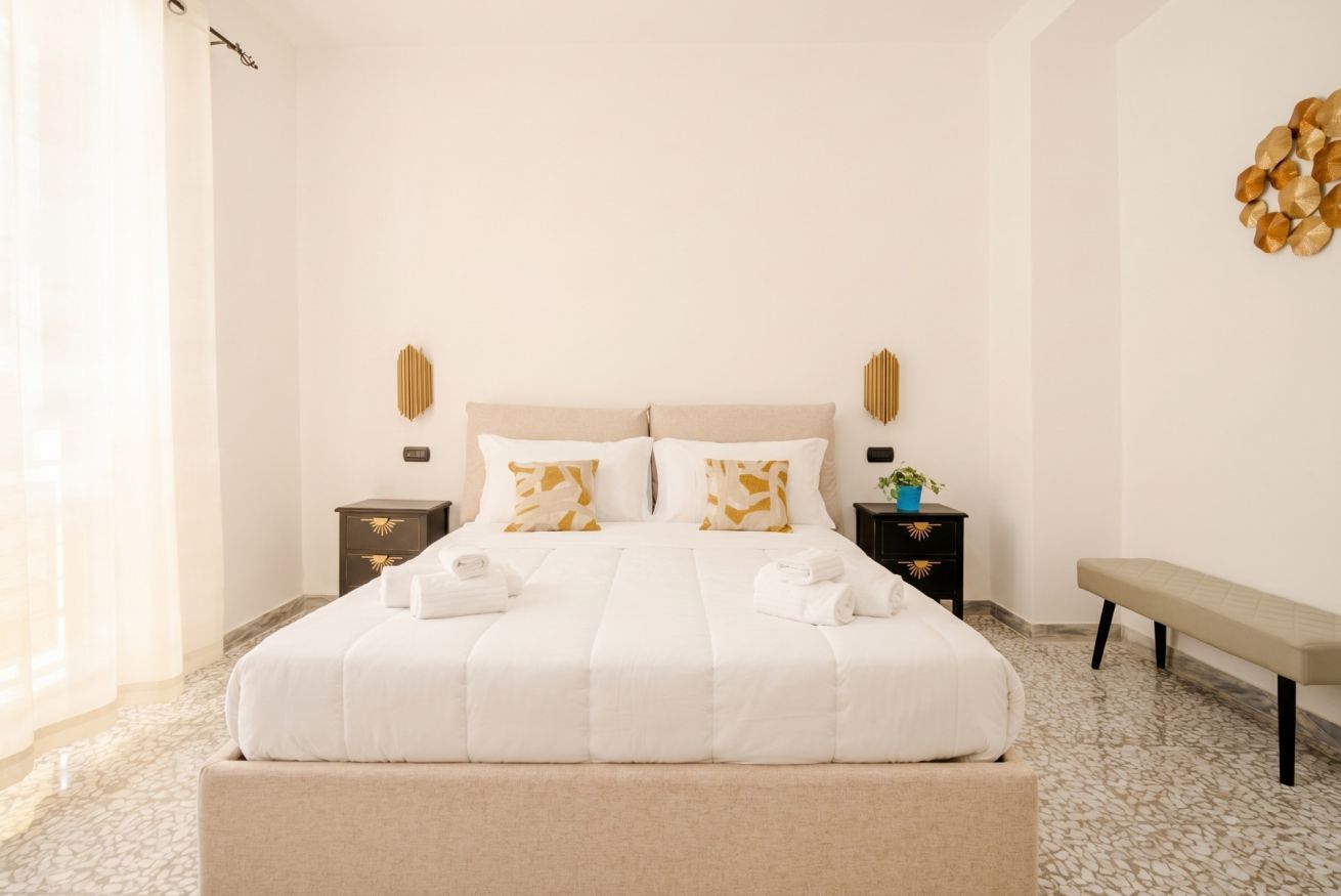 Een hotelkamer met een groot bed, nachtkastjes, een bankje en een decoratief object aan de muur.
