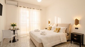 A bedroom with a bed, bedside tables, a desk with chairs, and a window with curtains.