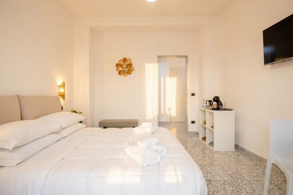Une chambre d’hôtel avec un grand lit, une table de chevet, un téléviseur fixé au mur et un petit coin salon.