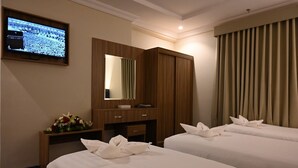 A hotel room with two beds, a TV mounted on the wall, a wooden desk with a mirror, and a window with curtains. - Durrat Al Jawar (Makkah)
