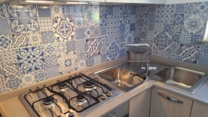 A kitchen with a gas stove, stainless steel sink, and patterned blue and white tiles. - La Campetella. Relaxation within walking distance of downtown. (Ischia)