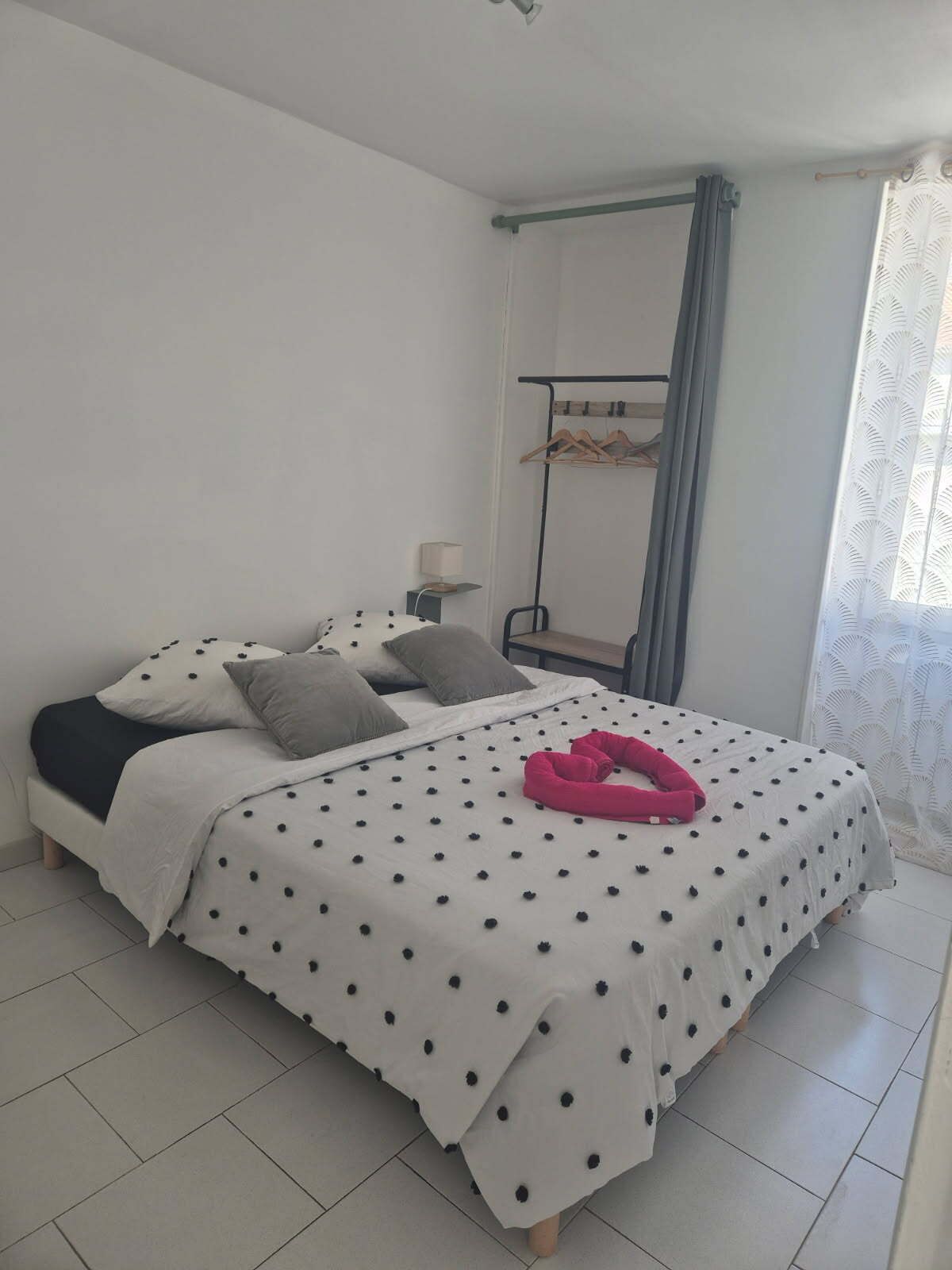 Un dormitorio con cama, almohadas, un perchero y una ventana con cortinas.