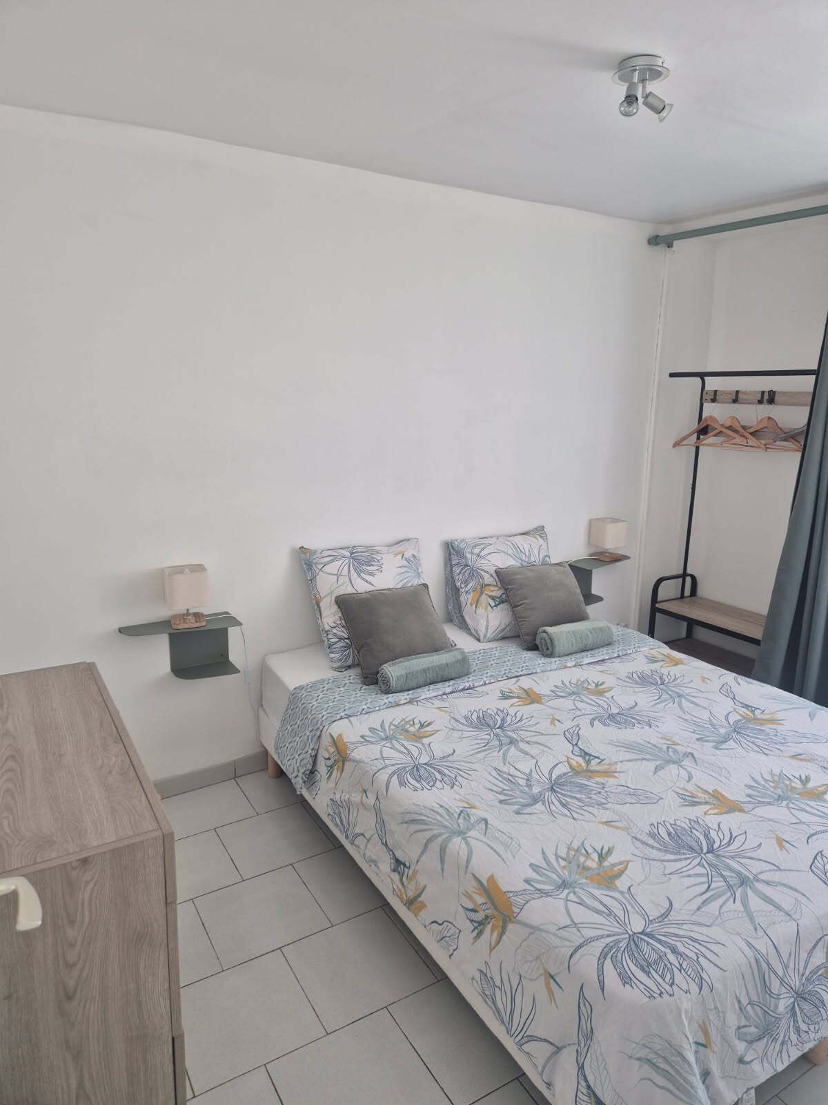 A bedroom with a bed, bedside tables, a hanging rack, and a wooden desk.