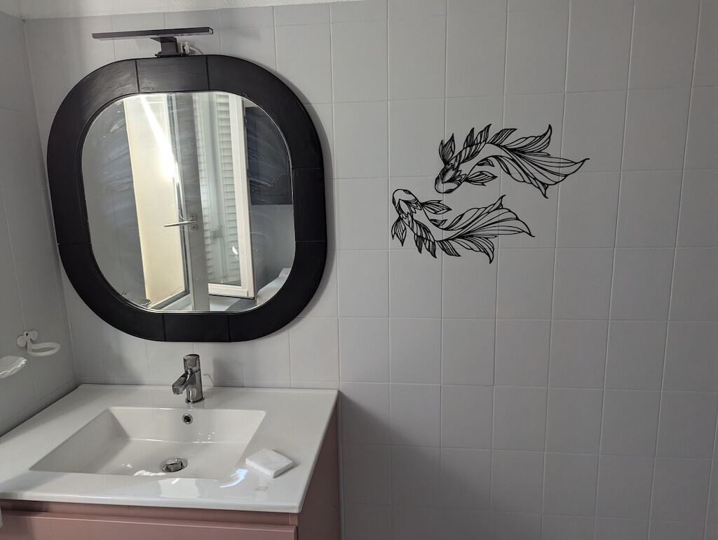 Un baño con un lavamanos blanco, un espejo con marco negro y decoración en la pared.