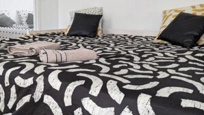 A bedroom with a patterned bedspread, two black pillows, a folded towel, and three framed artworks on the wall. - The Bangor Coon Apartment Liouba (Forges)