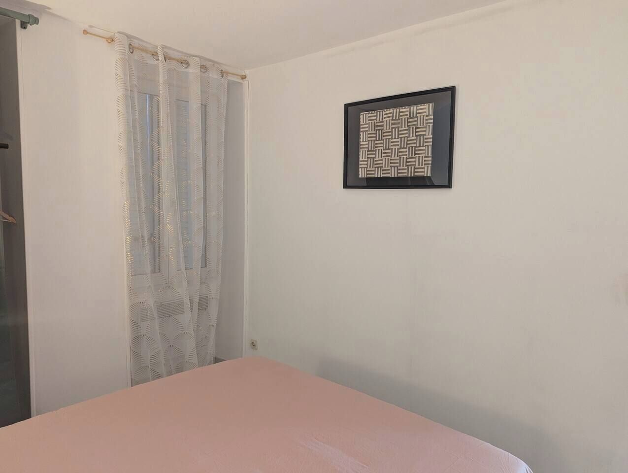 Een kamer met een bed, een gordijn met dessin en een lijst met afbeelding.
