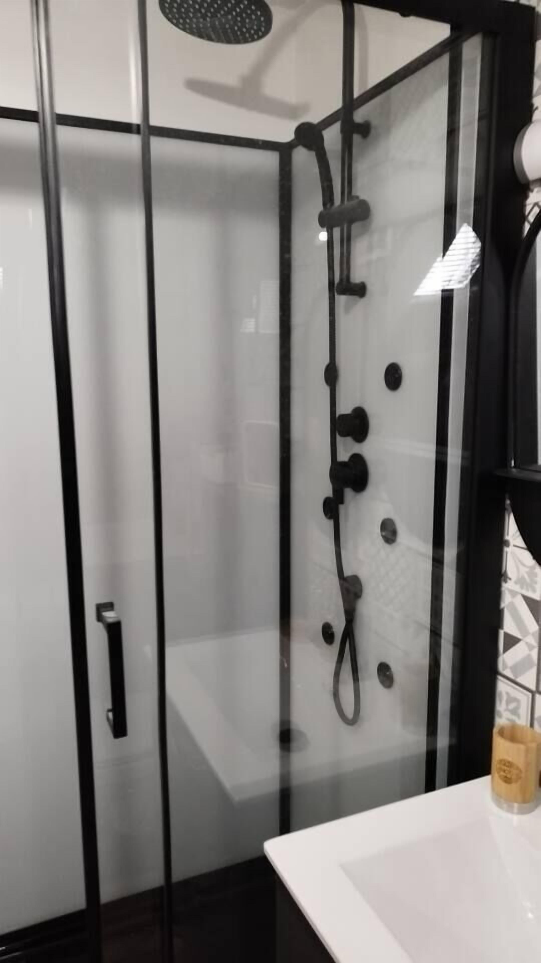 Un baño moderno con cabina de ducha de vidrio, un lavamanos blanco y un perchero.