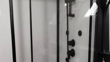 Un baño moderno con cabina de ducha de vidrio, un lavamanos blanco y un perchero.